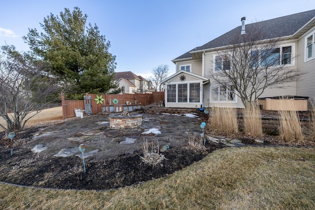 rear view of property featuring a sunroom, fence, and a fire pit