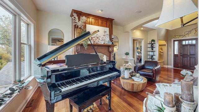 living area featuring ornate columns, baseboards, arched walkways, and wood finished floors