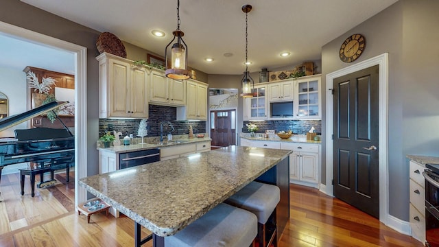 kitchen featuring a kitchen island, a kitchen breakfast bar, hardwood / wood-style floors, light stone countertops, and a sink