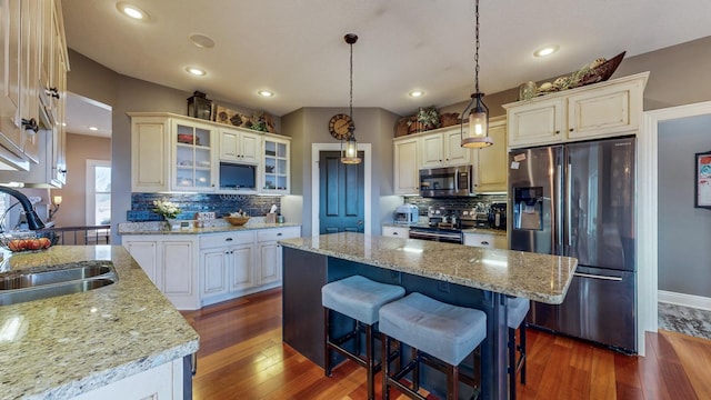 kitchen with glass insert cabinets, dark wood-type flooring, stainless steel appliances, a kitchen bar, and a sink