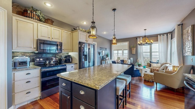 kitchen featuring appliances with stainless steel finishes, wood finished floors, a center island, a kitchen bar, and backsplash