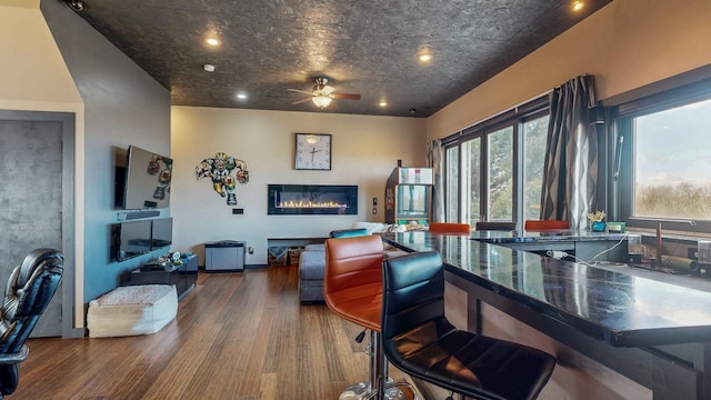 interior space featuring a glass covered fireplace, wood finished floors, and a ceiling fan