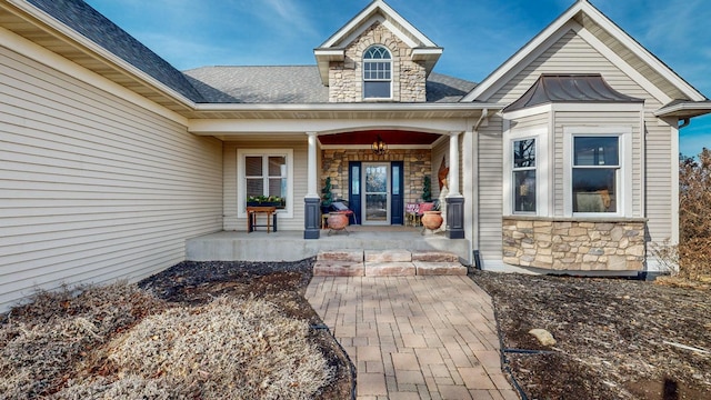 view of exterior entry featuring metal roof, a porch, a shingled roof, stone siding, and a standing seam roof