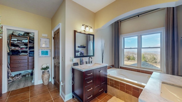 full bathroom featuring vanity, baseboards, tile patterned floors, a walk in closet, and a garden tub