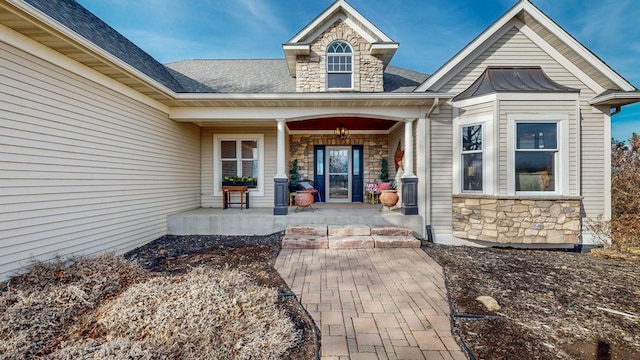 entrance to property with roof with shingles, covered porch, and stone siding