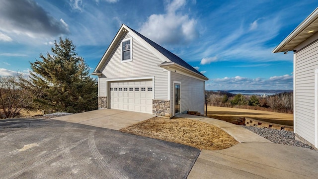 view of side of home with a garage, driveway, stone siding, and an outbuilding