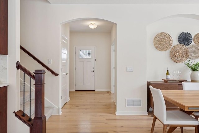 foyer entrance with arched walkways, visible vents, baseboards, light wood-style floors, and stairway