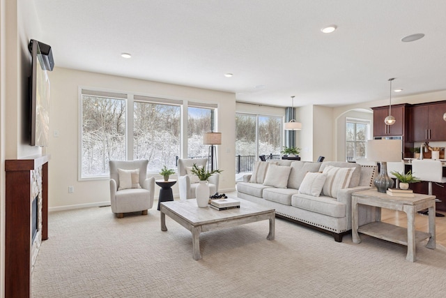 living area with arched walkways, a fireplace, recessed lighting, light colored carpet, and baseboards