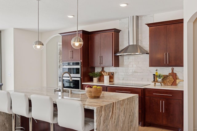 kitchen featuring tasteful backsplash, double oven, a sink, wall chimney exhaust hood, and black electric cooktop