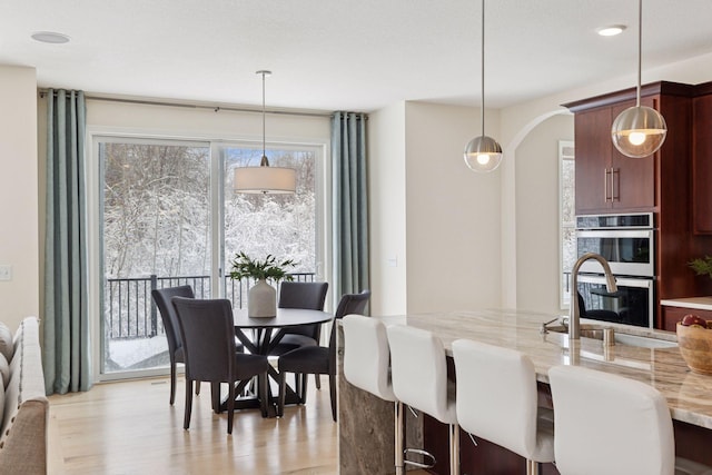 dining space featuring plenty of natural light, arched walkways, and light wood-style flooring