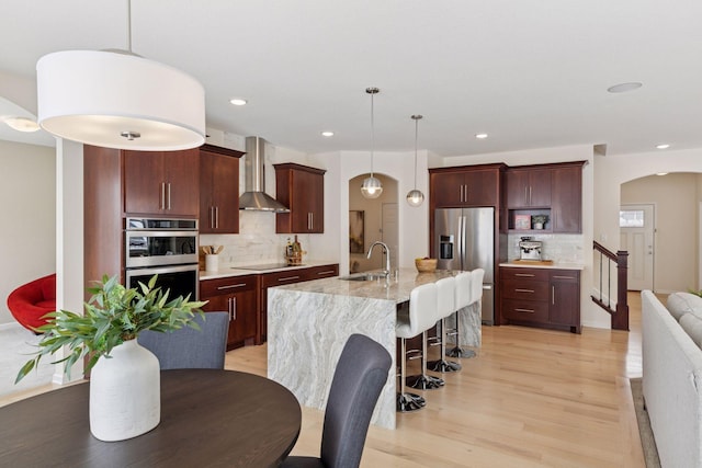 kitchen with light wood-style flooring, a kitchen breakfast bar, stainless steel appliances, wall chimney range hood, and a sink