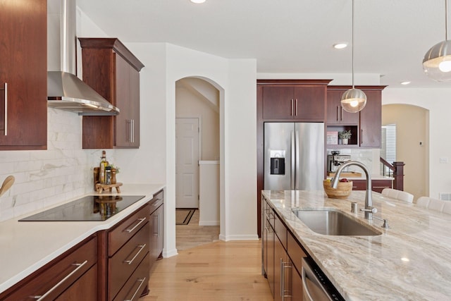 kitchen featuring black electric cooktop, a sink, wall chimney range hood, stainless steel fridge with ice dispenser, and decorative light fixtures