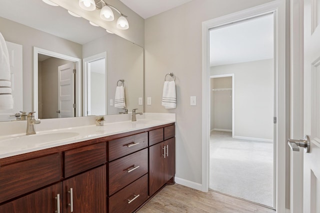 full bathroom with wood finished floors, a sink, baseboards, and double vanity