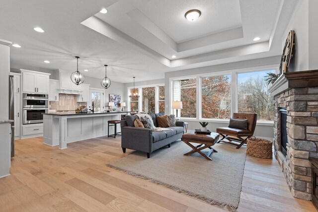 22816 Jarvis St NW, Elk River, MN 55330 - living room featuring a fireplace, a notable chandelier, a tray ceiling, a healthy amount of sunlight, and light wood-type flooring