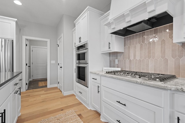 22816 Jarvis St NW, Elk River, MN 55330 - kitchen featuring tasteful backsplash, white cabinetry, stainless steel appliances, light wood-type flooring, and wall chimney exhaust hood