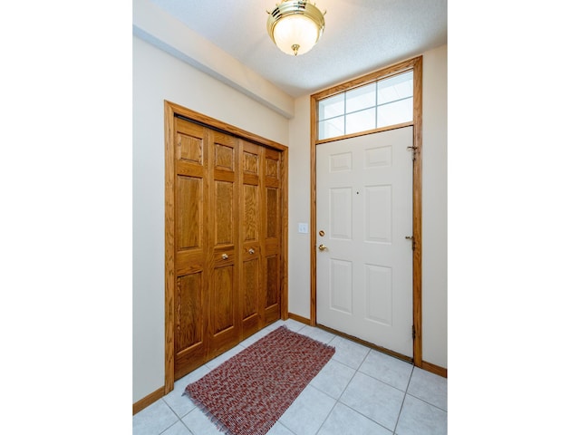 entrance foyer with light tile patterned floors, a textured ceiling, and baseboards