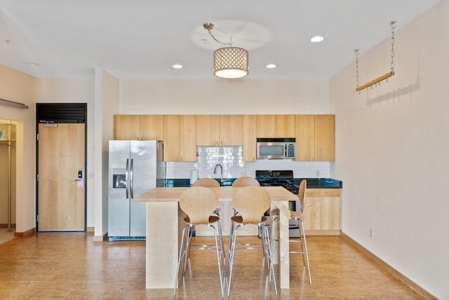 kitchen featuring appliances with stainless steel finishes, tasteful backsplash, a kitchen island, decorative light fixtures, and light brown cabinets