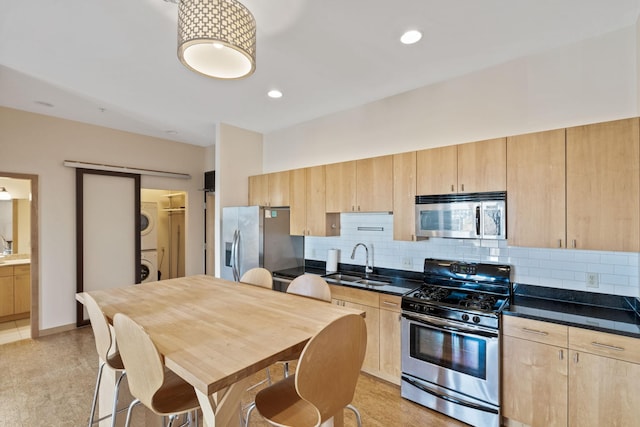 kitchen with appliances with stainless steel finishes, stacked washer / drying machine, sink, and light brown cabinets