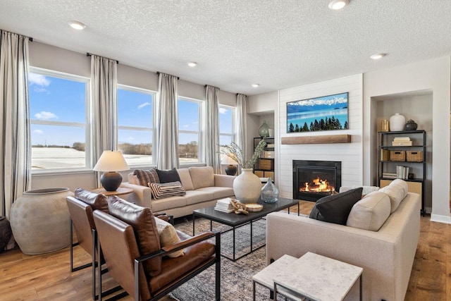 living room featuring a textured ceiling, built in shelves, recessed lighting, a fireplace, and light wood-style floors