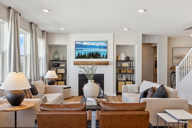 living area with a textured ceiling, recessed lighting, a fireplace, stairs, and light wood-type flooring