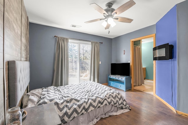 bedroom with visible vents, baseboards, ceiling fan, wood finished floors, and ensuite bath