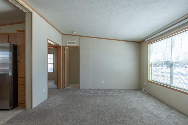 spare room featuring a textured ceiling, a healthy amount of sunlight, visible vents, and crown molding