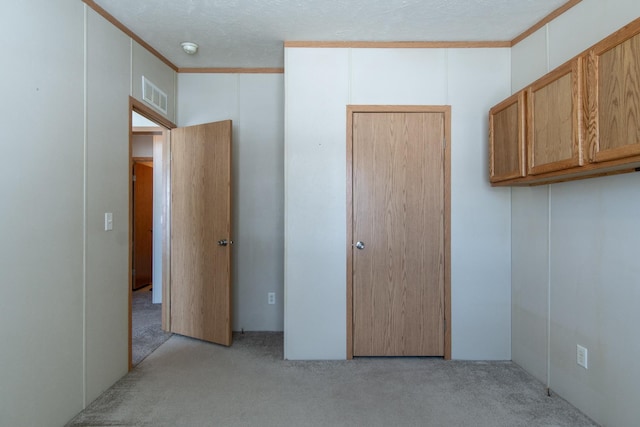 unfurnished bedroom featuring a textured ceiling, ornamental molding, visible vents, and light colored carpet