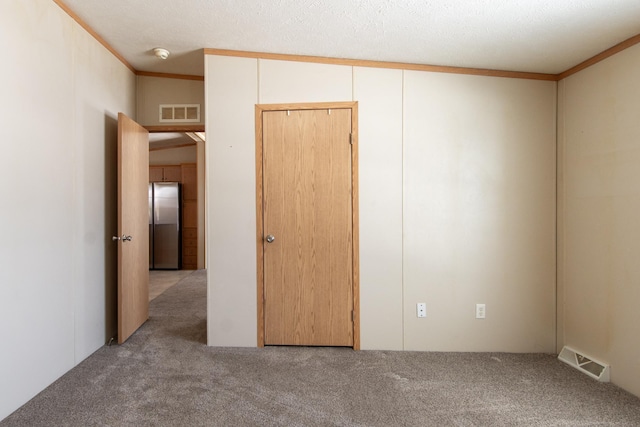 unfurnished bedroom with a textured ceiling, visible vents, crown molding, and light colored carpet