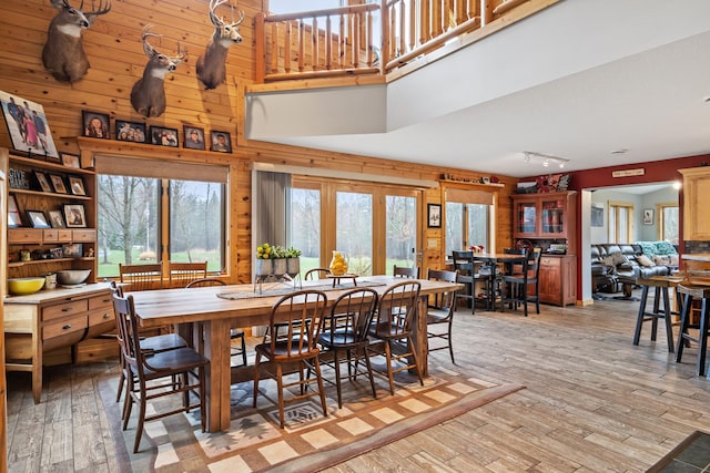 dining area with wood walls, track lighting, a high ceiling, and light wood-type flooring