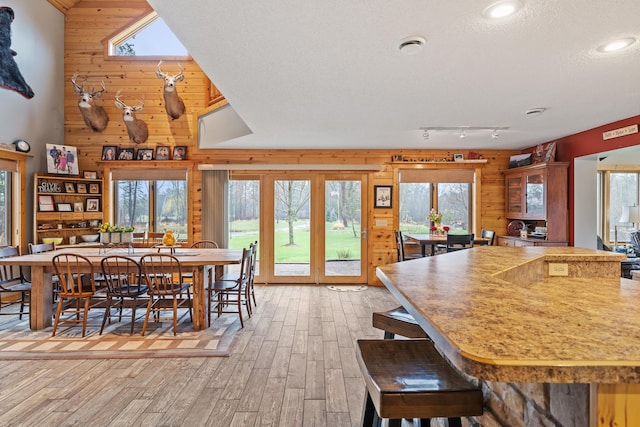 dining space featuring wooden walls, a high ceiling, light hardwood / wood-style flooring, and a textured ceiling