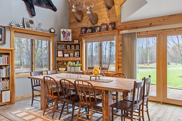 dining area featuring high vaulted ceiling, light wood-type flooring, plenty of natural light, and wooden walls