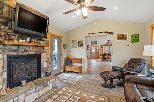 living room with hardwood / wood-style floors, lofted ceiling, ceiling fan, and a stone fireplace