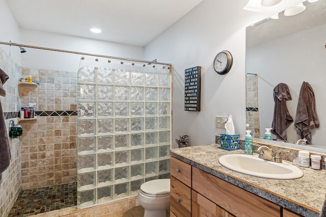 bathroom with toilet, a tile shower, and vanity