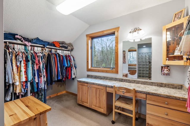 walk in closet with lofted ceiling, built in desk, and light colored carpet