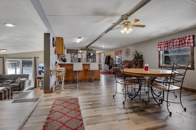 dining area featuring ceiling fan, indoor bar, light hardwood / wood-style floors, and lofted ceiling with beams