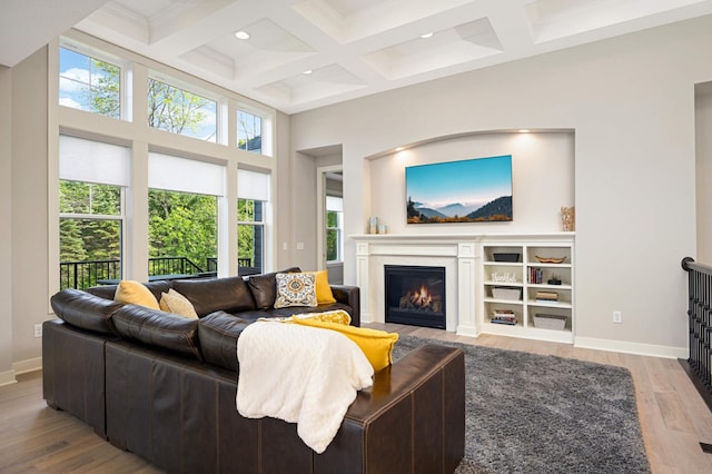 living room with beamed ceiling, coffered ceiling, light hardwood / wood-style floors, and a high ceiling