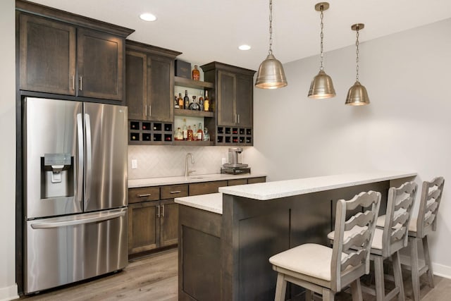 bar featuring hanging light fixtures, dark brown cabinets, stainless steel refrigerator with ice dispenser, light hardwood / wood-style floors, and decorative backsplash