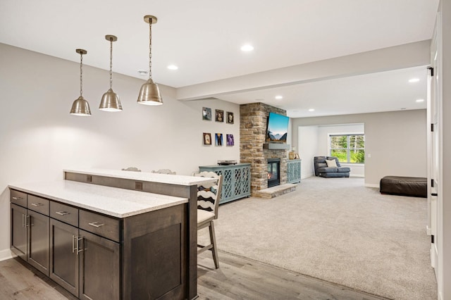 kitchen featuring a kitchen bar, a stone fireplace, light stone counters, hanging light fixtures, and dark brown cabinets