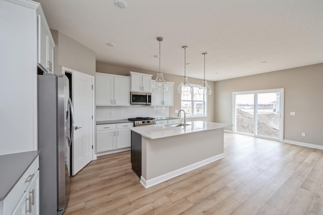 kitchen featuring appliances with stainless steel finishes, white cabinetry, backsplash, a center island with sink, and decorative light fixtures