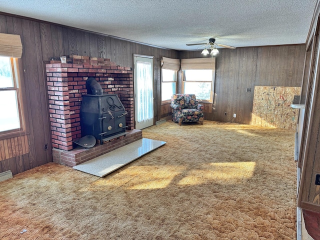 unfurnished living room featuring light carpet, wooden walls, a textured ceiling, and a wood stove