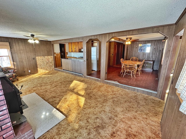 carpeted living room featuring ceiling fan, wooden walls, and a textured ceiling