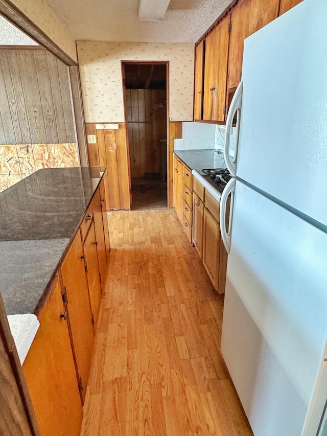 kitchen featuring wooden walls, dark stone counters, white refrigerator, light hardwood / wood-style floors, and a textured ceiling