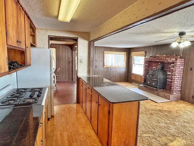 kitchen with a wood stove, ceiling fan, gas stovetop, a textured ceiling, and light wood-type flooring