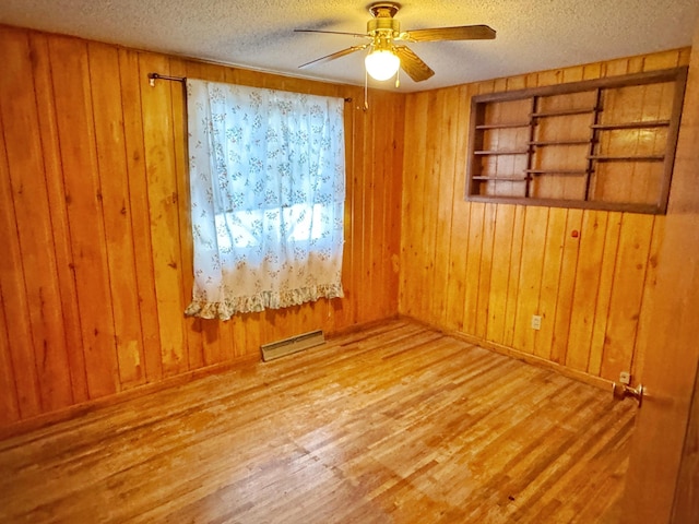 spare room with wood-type flooring, ceiling fan, a textured ceiling, and wooden walls