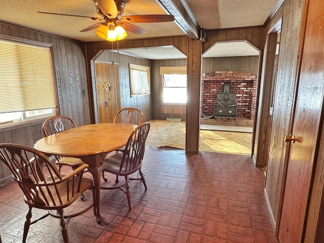 dining room featuring ceiling fan, a wood stove, a textured ceiling, and wooden walls