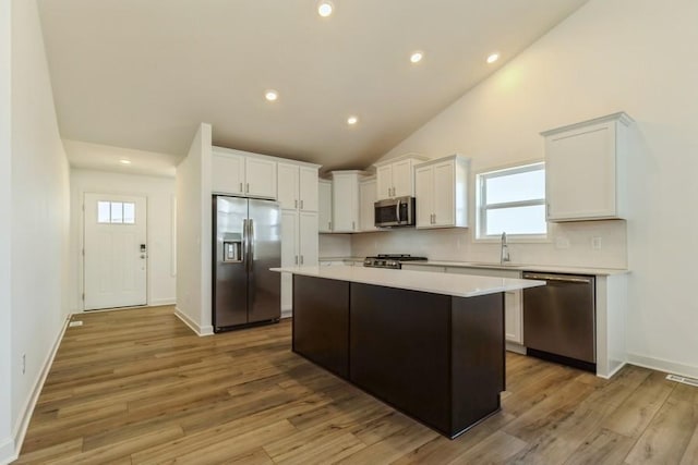 kitchen with sink, white cabinetry, stainless steel appliances, a center island, and light wood-type flooring