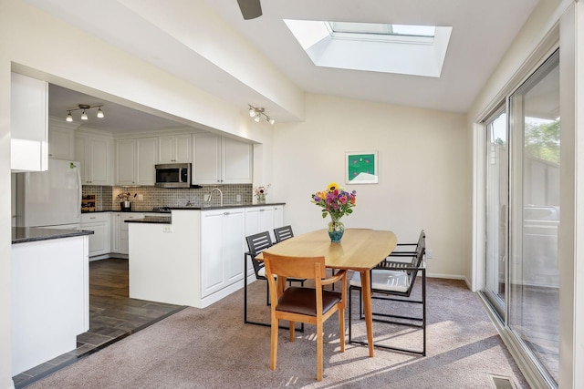 dining space with lofted ceiling with skylight and dark colored carpet