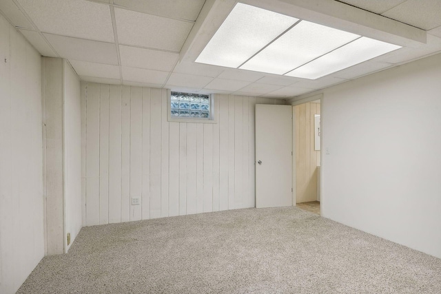 basement featuring carpet, a drop ceiling, and wooden walls