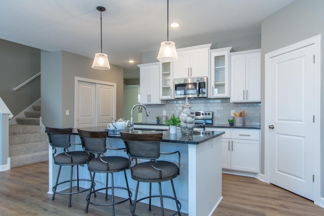 kitchen featuring sink, white cabinets, hanging light fixtures, stainless steel appliances, and a center island with sink