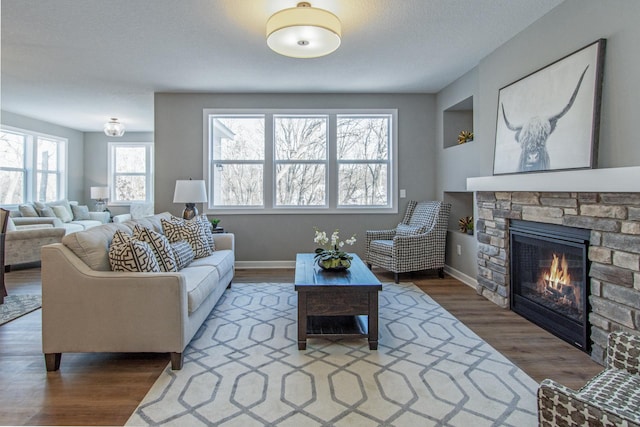 living room featuring wood-type flooring, a stone fireplace, and a textured ceiling